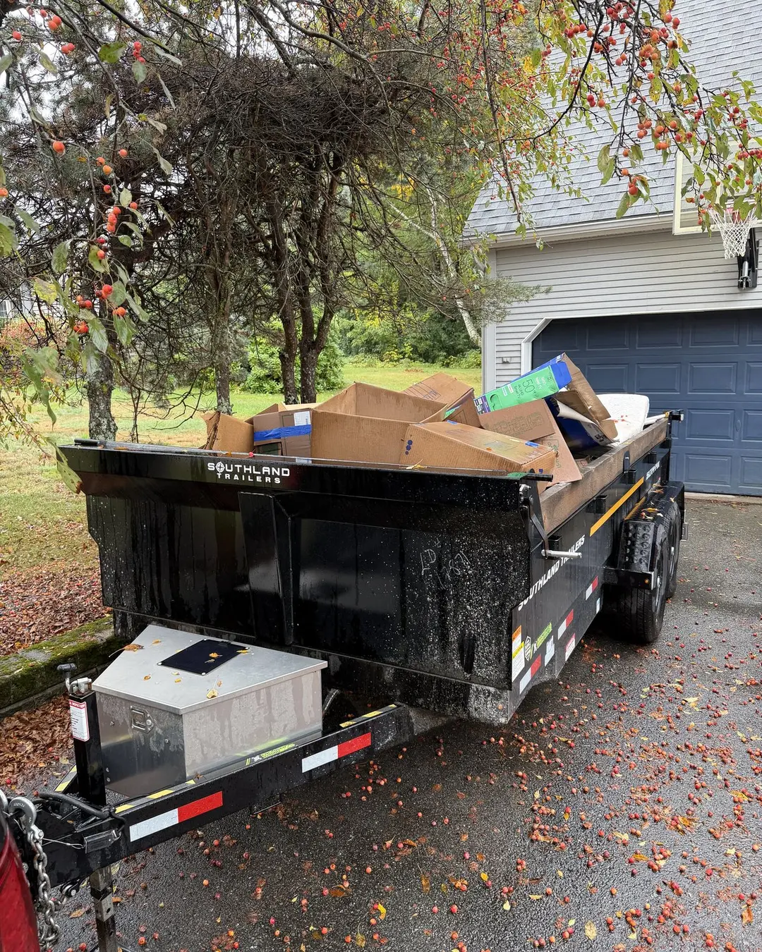 Trailer loaded with household items beside a garage